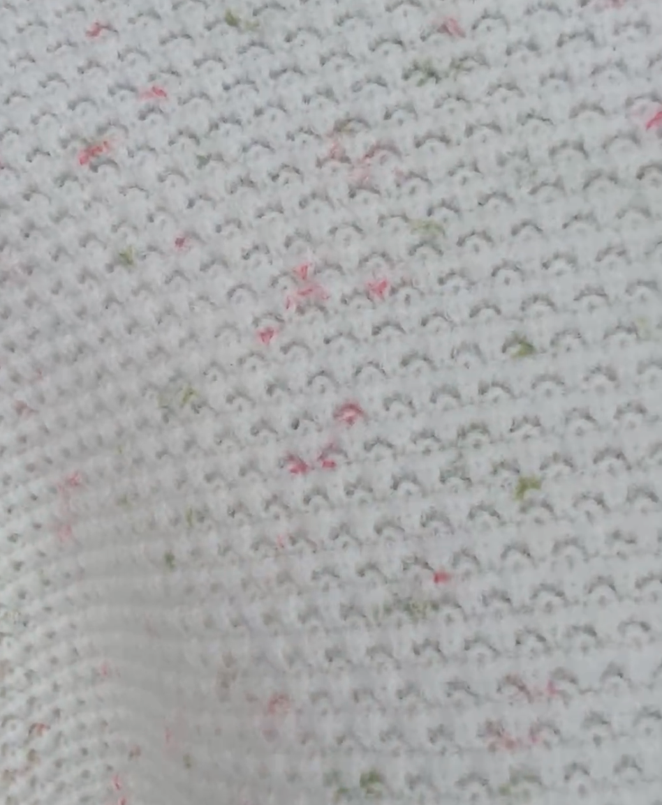 Pink and Green: Close-up of a textured white fabric with small red and green specks
